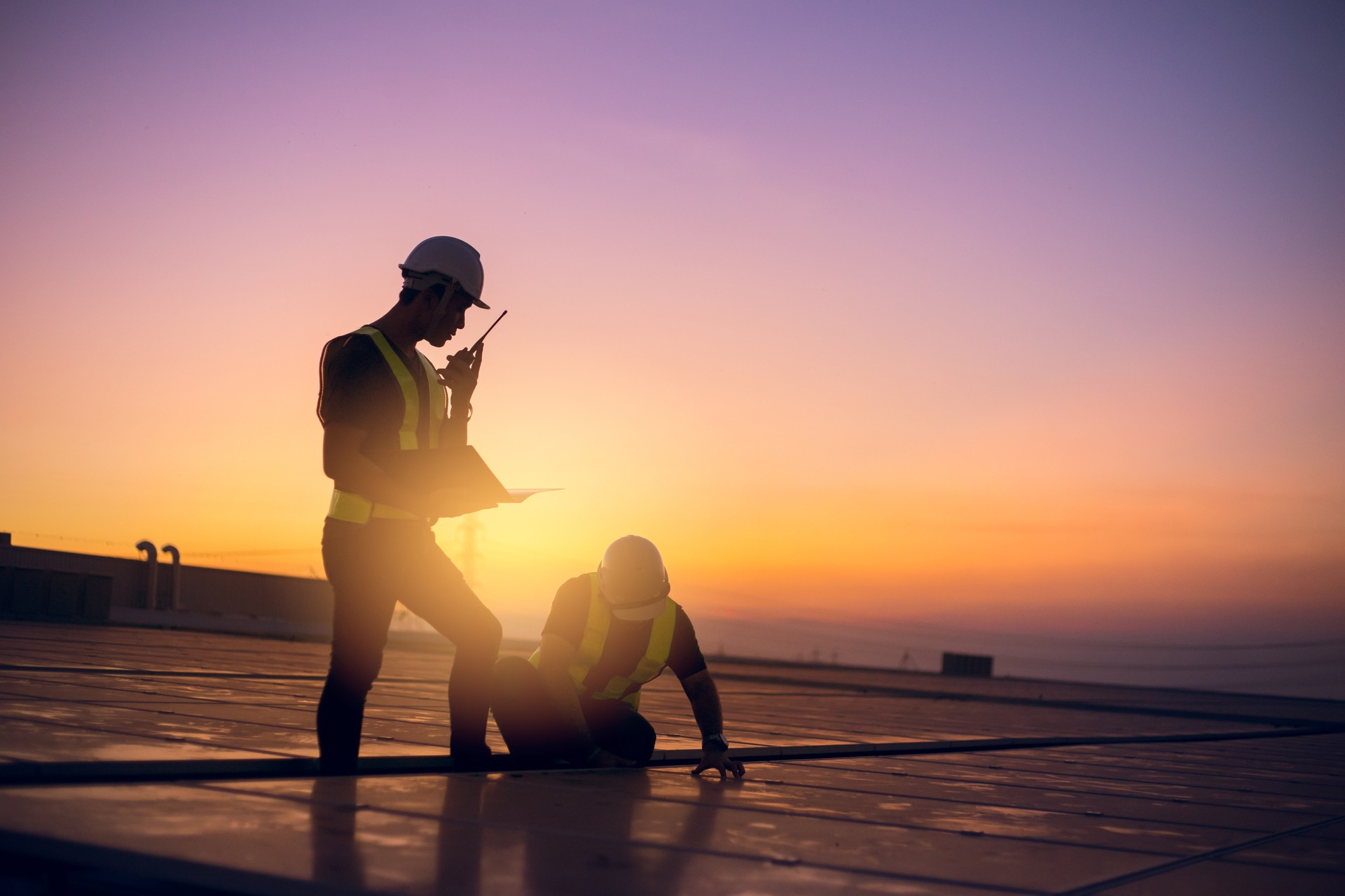 Two technicians service yearly preventive maintenance solar cells on roof factory under morning sunlight.